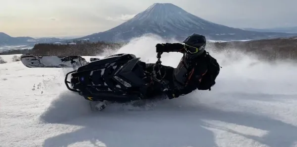 Rider kicking up powder on a snowmobile with Mt Yotei behind