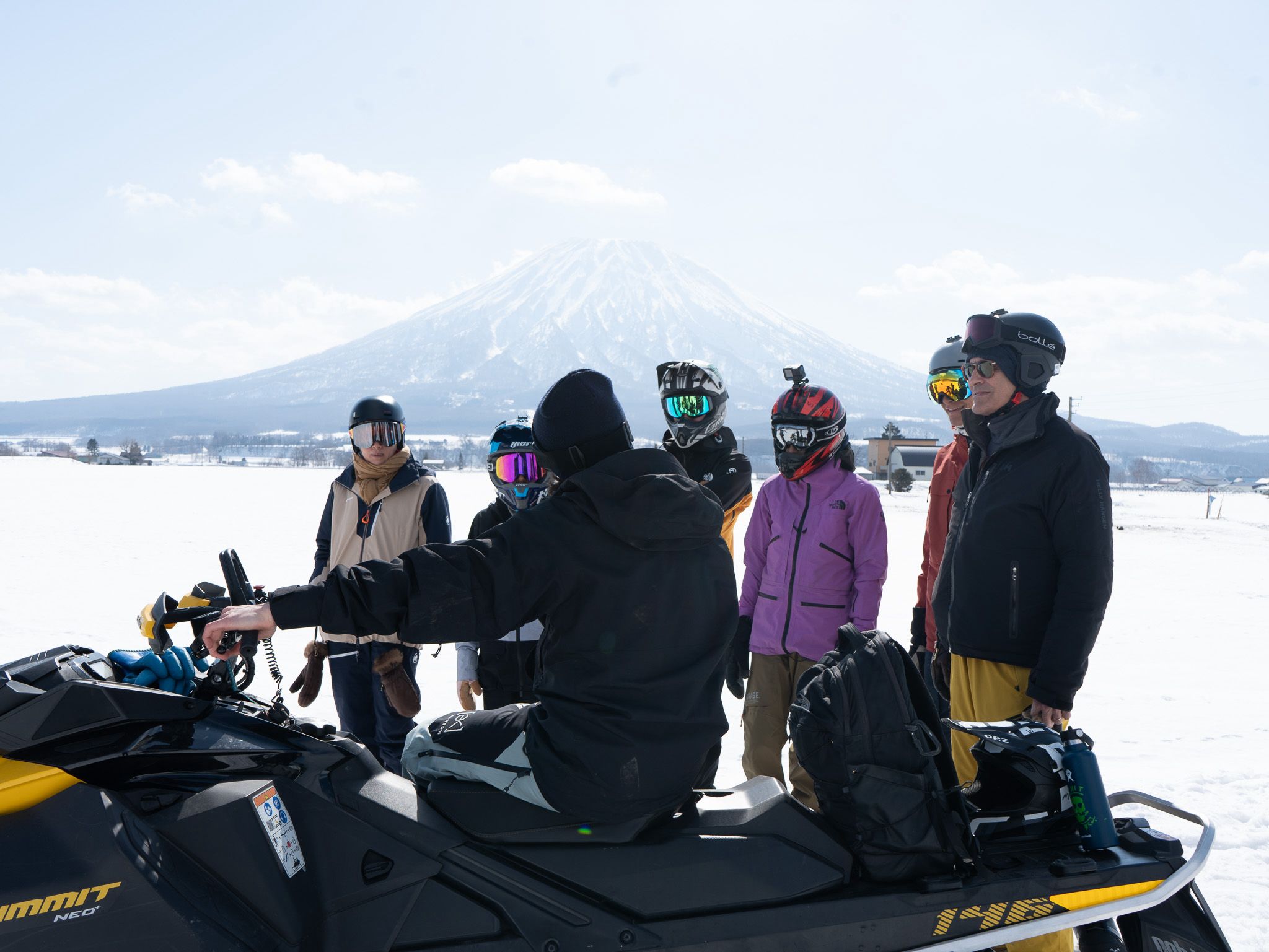 Guide giving a safety briefing to a group of snowmobile riders with Mt Yotei behind them
