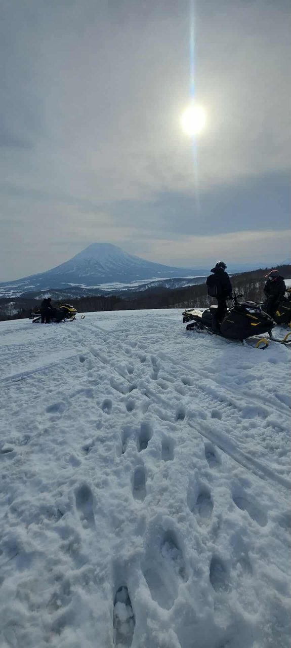 Snowmobile riders on a Niseko ridge with the sun breaking over the snow